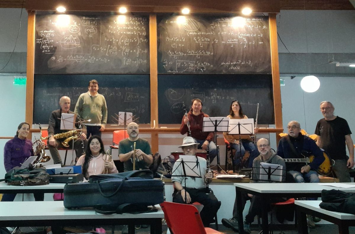 The Banda Atómica wind band posing with their instruments in a classroom, in front of blackboards full of equations